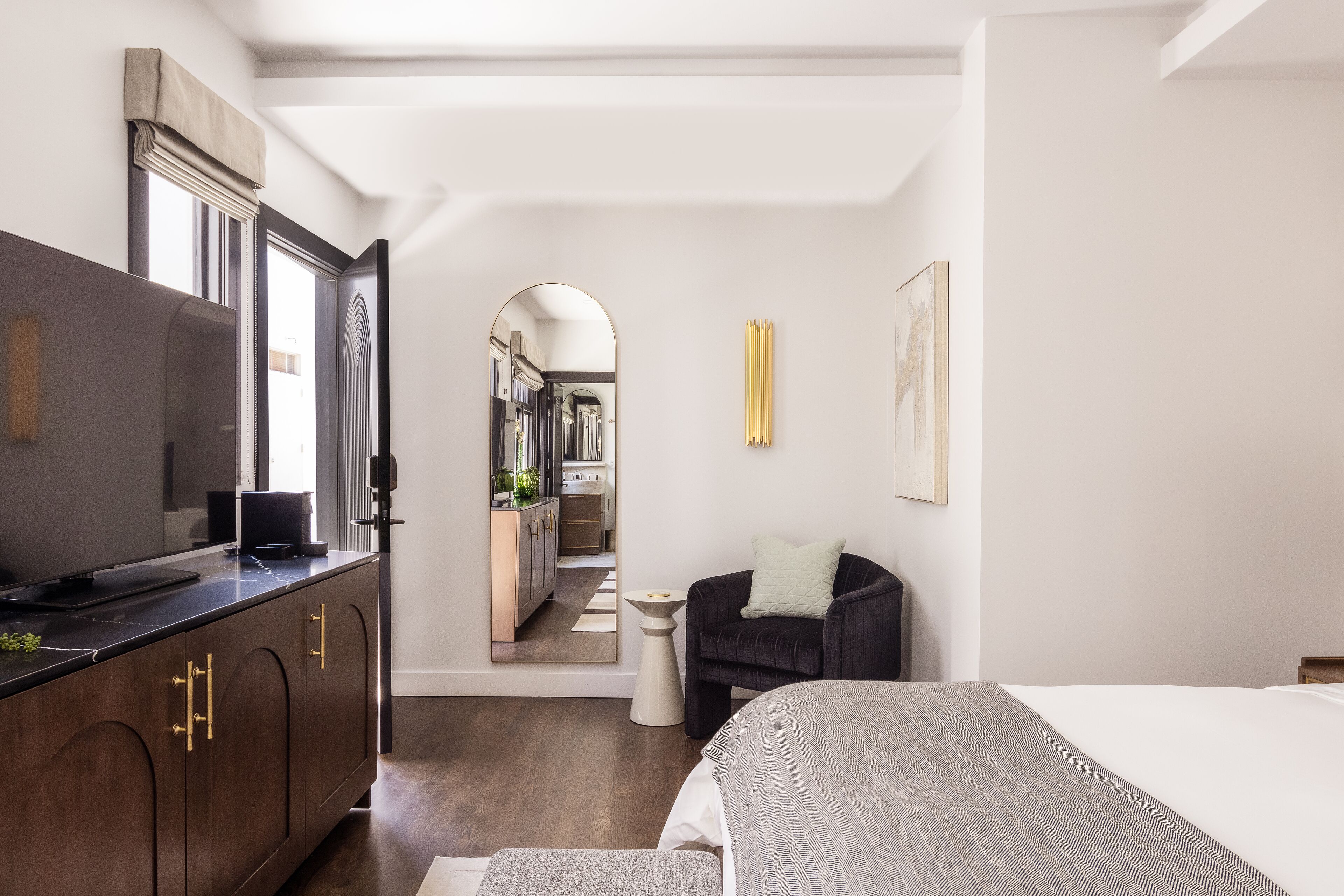 Un dormitorio moderno con una cama, un sillón oscuro, una mesita de noche, un espejo y un armario.