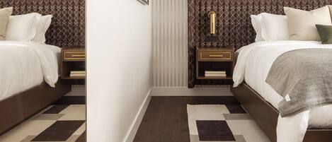 A bedroom with two beds, a nightstand with a lamp, and a patterned rug.