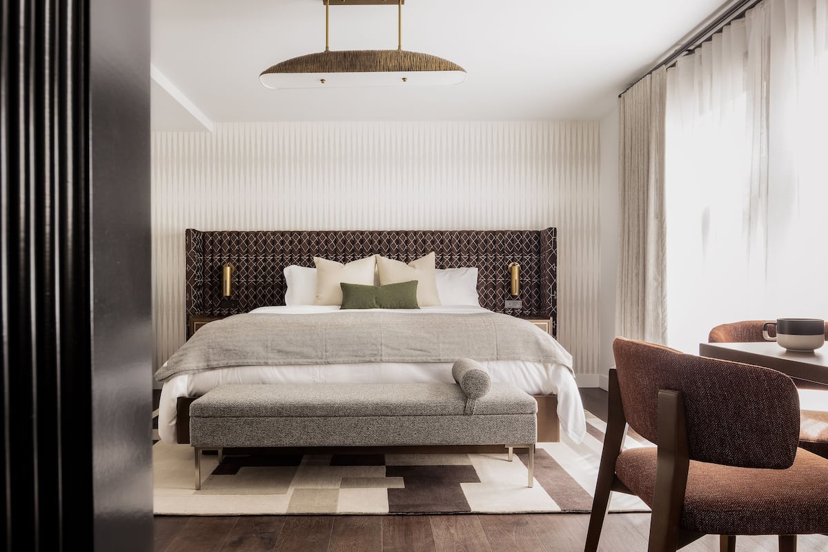 A modern bedroom with a large bed, a bench, a chair, and a table.