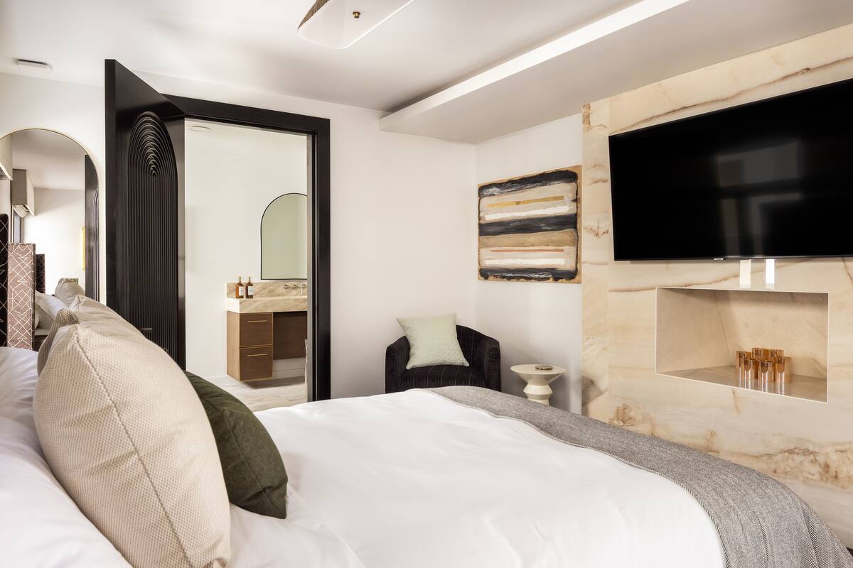 A modern bedroom with a large bed, a TV mounted on the wall, and a bathroom vanity.