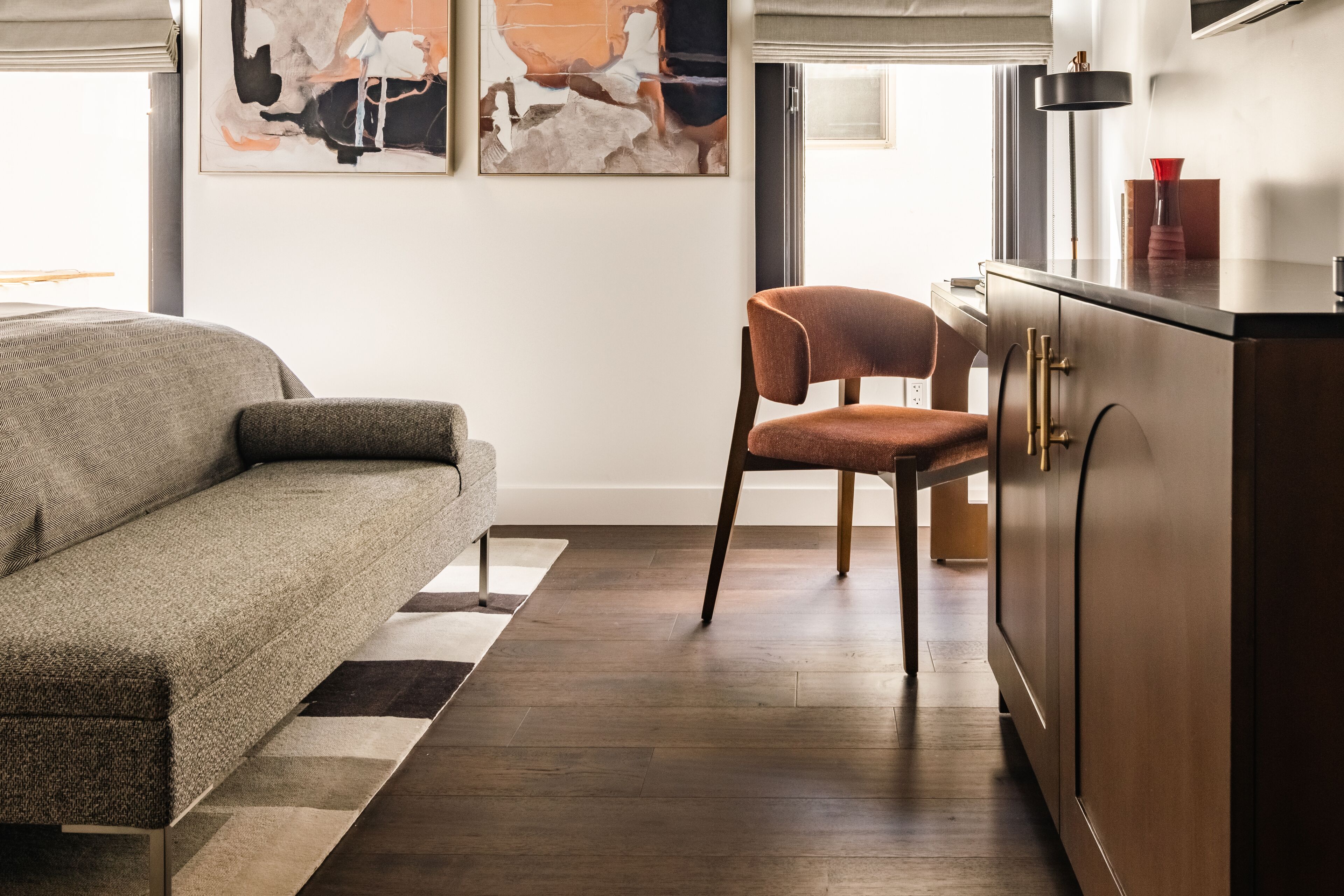 A modern living room with a sofa, a chair, a cabinet, and abstract art on the wall.