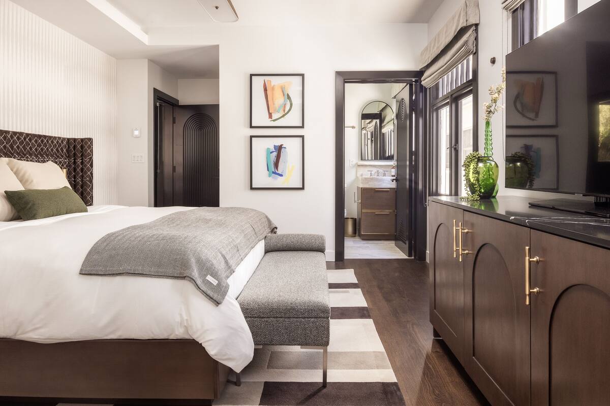 A modern bedroom with a large bed, a bench, and a dark wooden wardrobe.