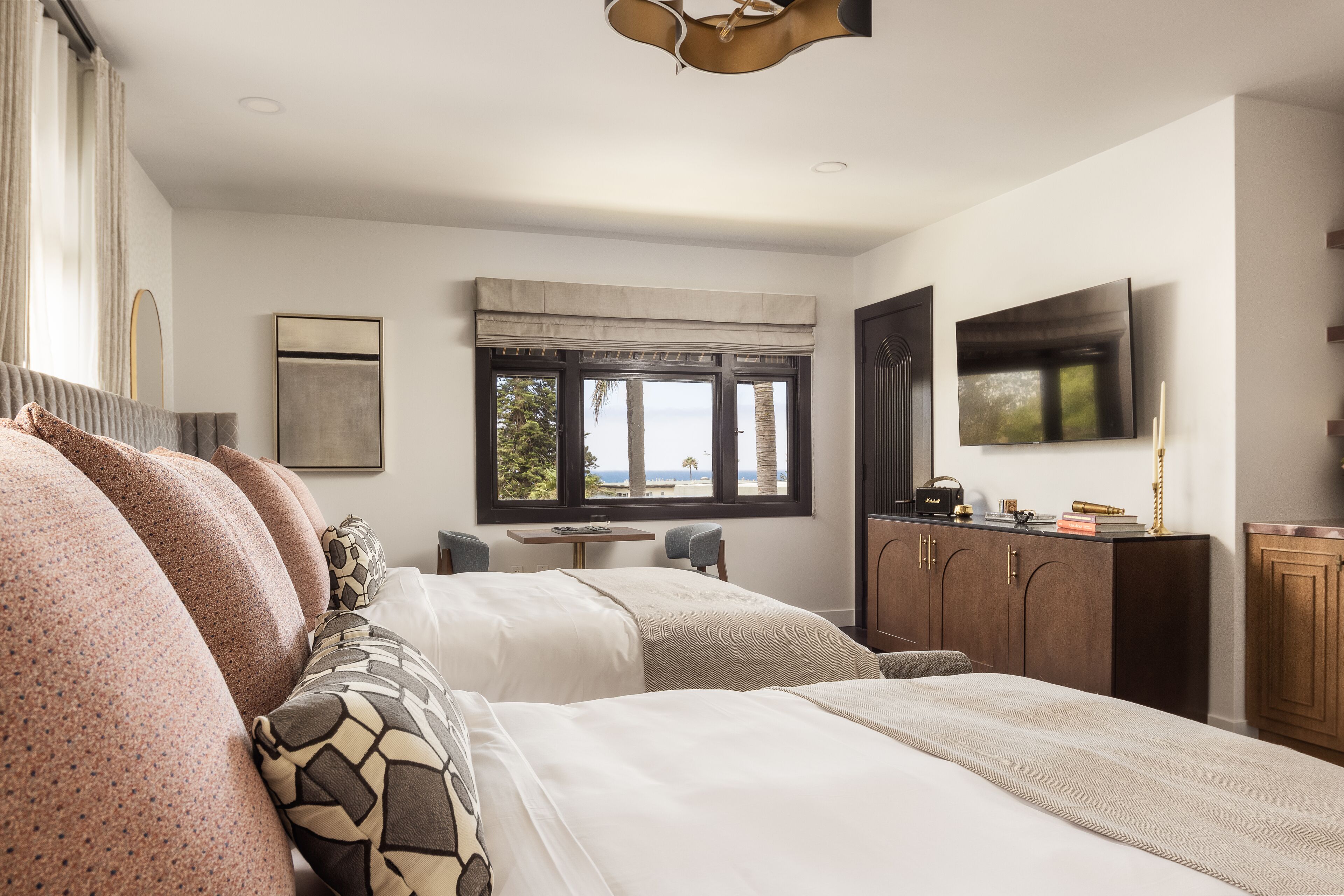 Habitación de hotel moderna con dos camas, televisión, escritorio y vistas al exterior.