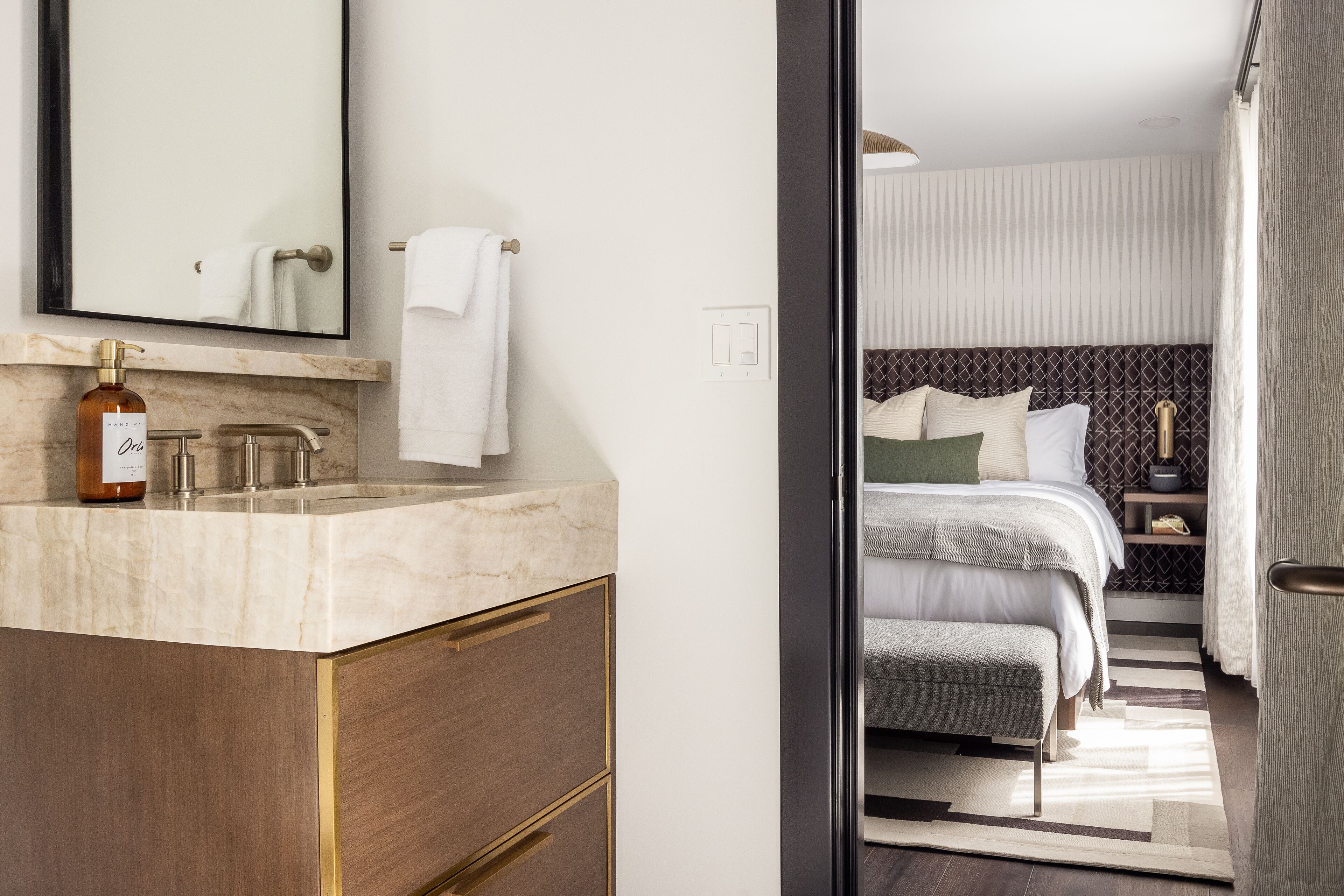 A modern bathroom with a marble sink, a bottle of lotion, and a large mirror.