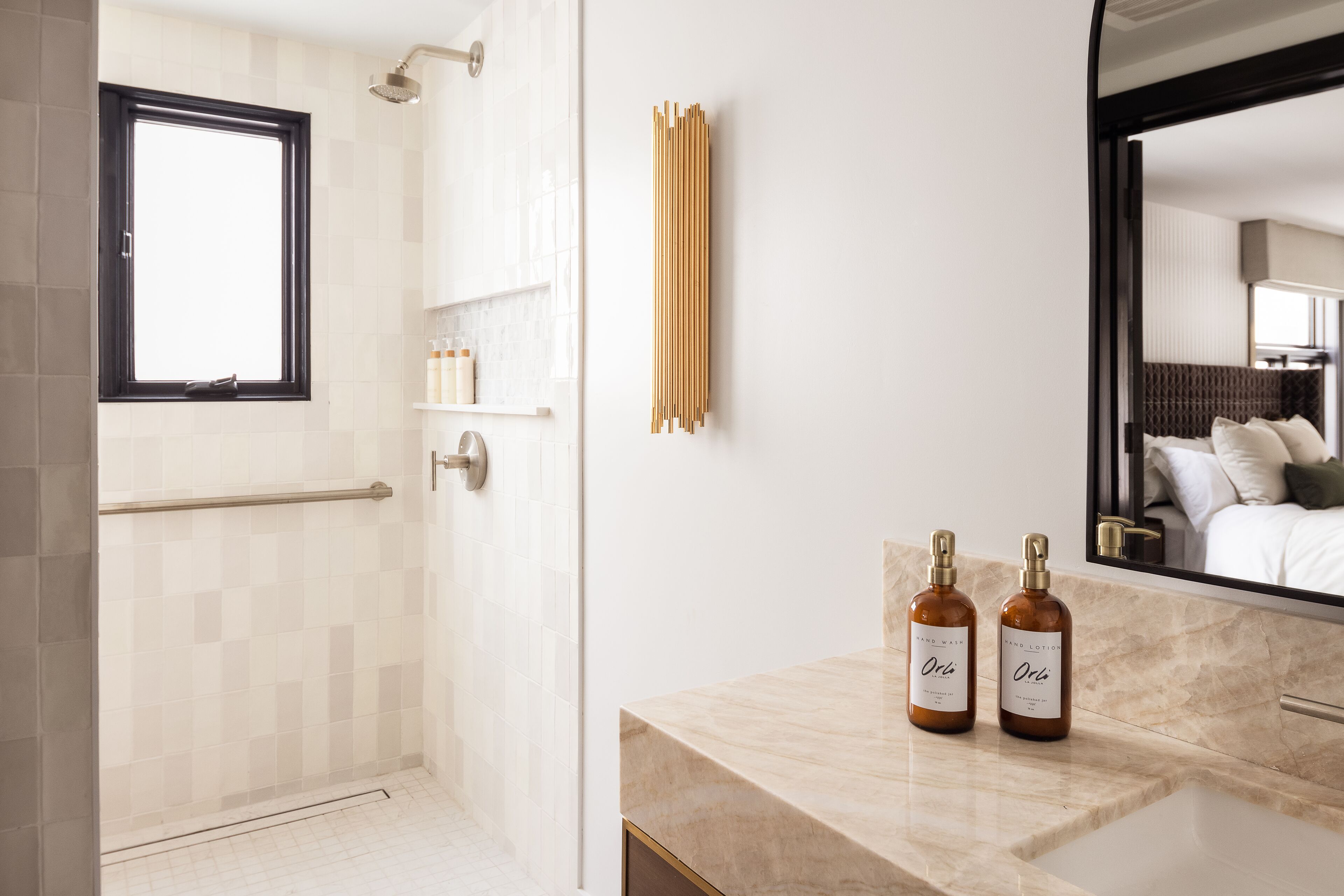 Een moderne badkamer met een douche, een wastafel met een marmeren blad en twee flesjes Orla body lotion.