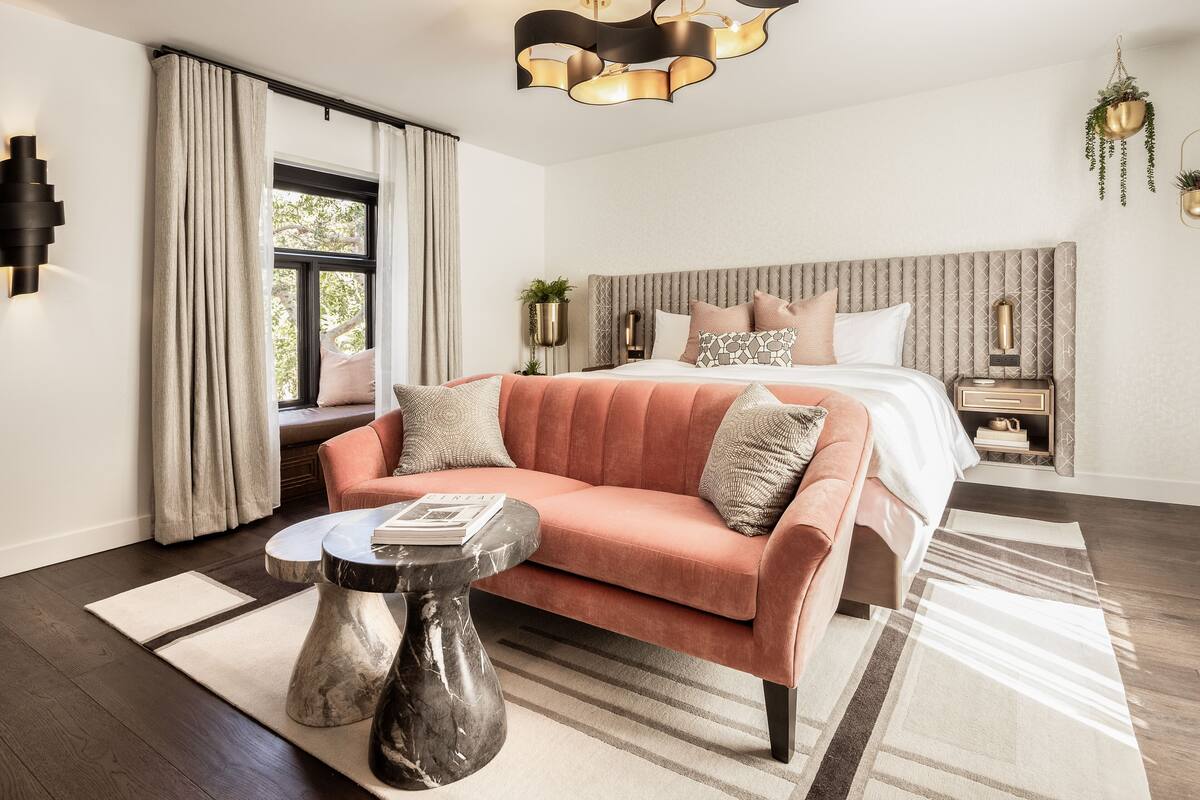 A modern bedroom with a large bed, a sofa, a side table, and a hanging plant.