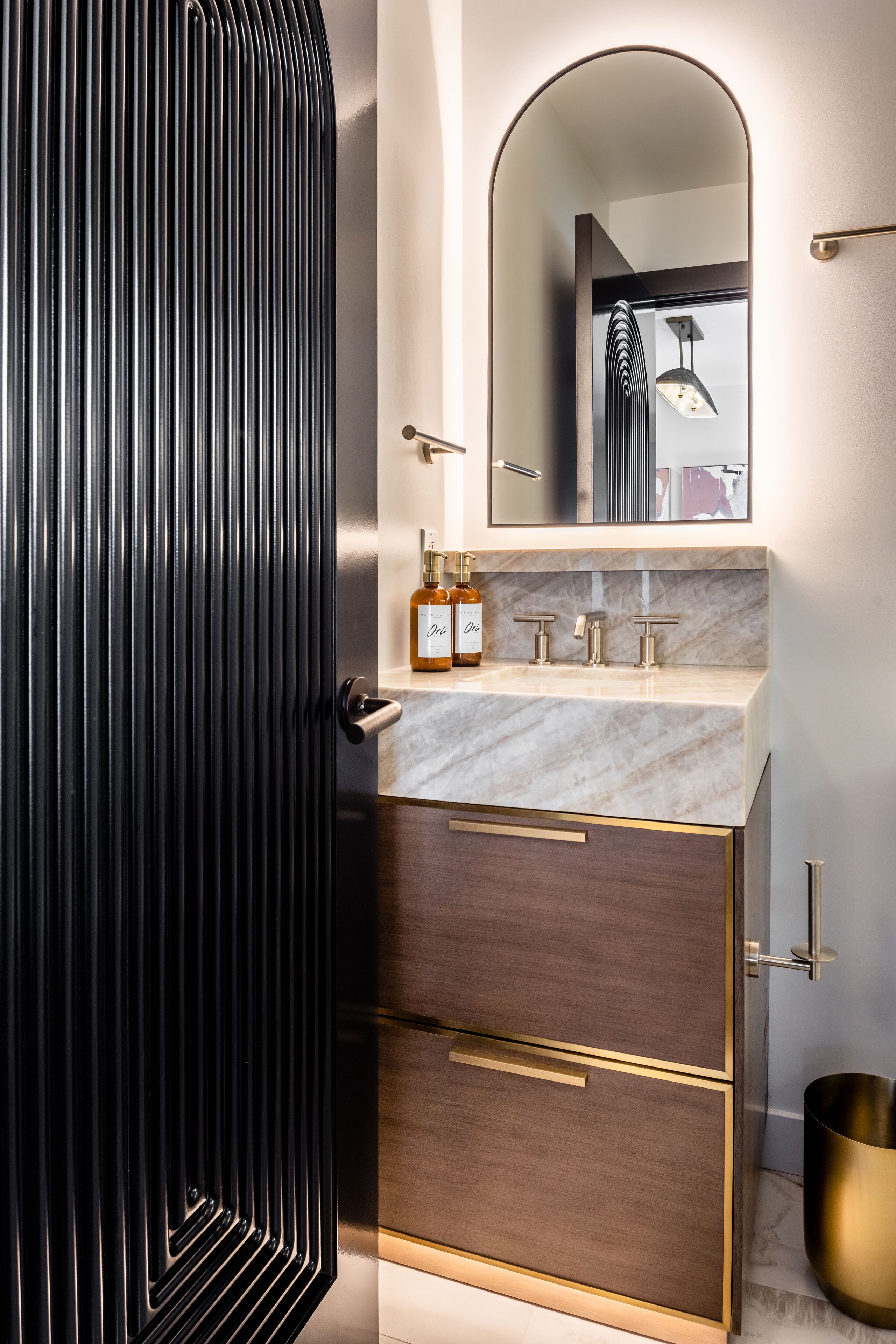 Un baño moderno con tocador de mármol, un espejo grande y una puerta negra con líneas verticales.