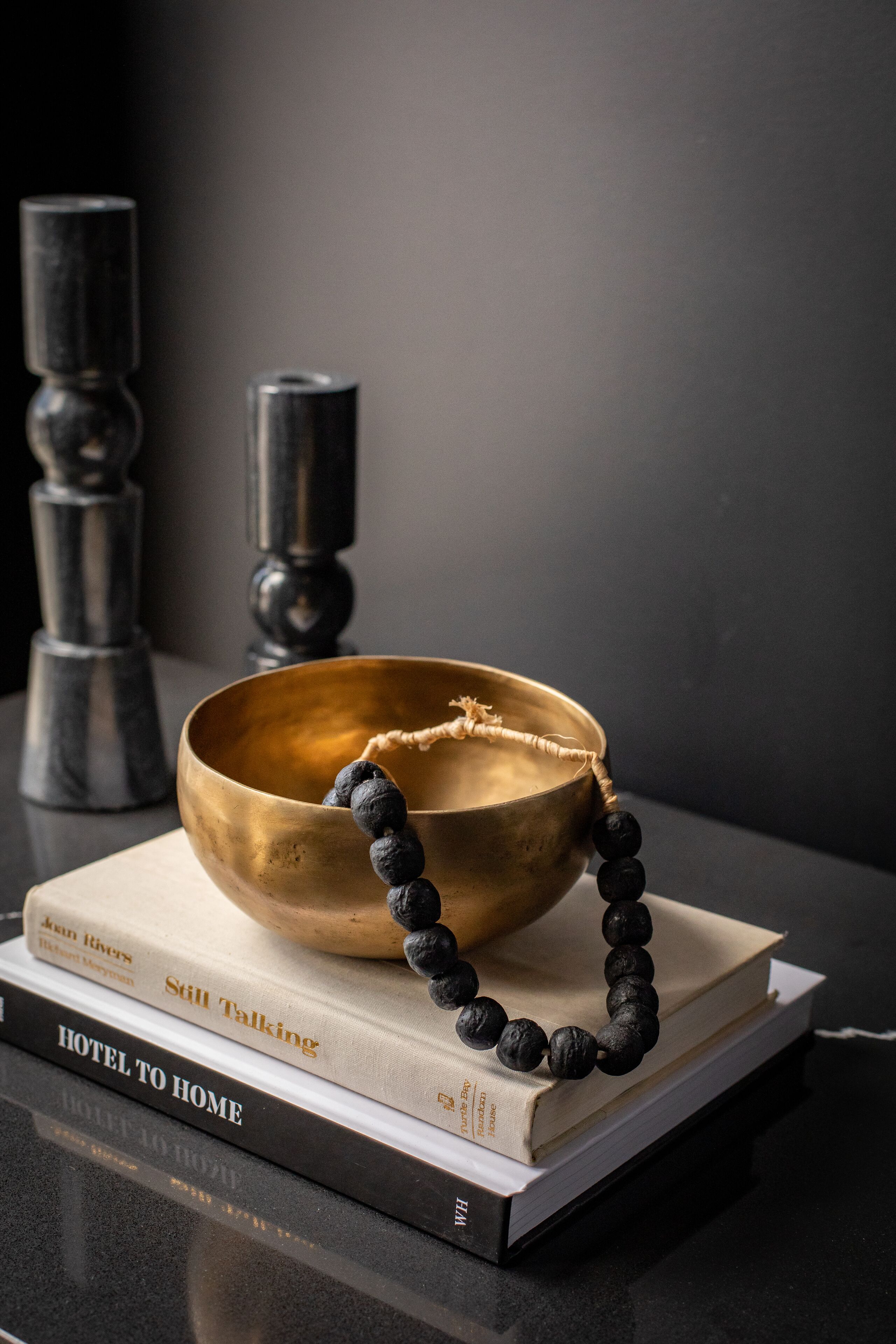 Un bol en laiton surmonté d’un collier noir orné de perles, le tout posé sur une pile de livres.