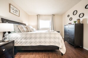 A neatly arranged bedroom with a bed, bedside table, dresser, and a wall clock. - ❤Cozy in the Springs! 2 BR, Kitchen. 4 Guests!❤ (Colorado Springs)