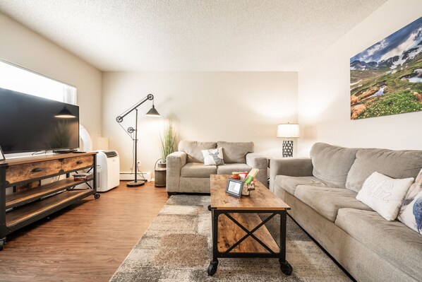 A living room with a large flat-screen TV, two sofas, a coffee table, and a floor lamp. - ❤Cozy in the Springs! 2 BR, Kitchen. 4 Guests!❤ (Colorado Springs)