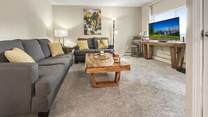 Un salon moderne avec un canapé gris, une table basse en bois et un téléviseur posé sur un meuble en bois.