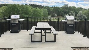 Une terrasse extérieure équipée de deux barbecues, d’une table de pique-nique et d’une clôture en métal noir.