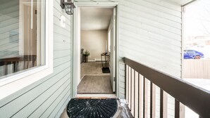 En smal, avskärmad veranda med ett träräcke, en dörrmatta och ett litet bord med en växt.