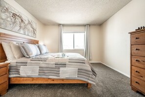 Un dormitorio con cama de madera, mesita de noche, cómoda y ventana con cortinas.
