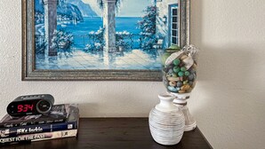 A framed painting of a coastal scene with arches, a table with books, a clock, and a decorative vase. - Beauty in the Springs"Entire Condo Great Location (Colorado Springs)