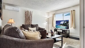 A living room with a sofa, a coffee table, a TV, and a painting of a beach scene. - Beauty in the Springs"Entire Condo Great Location (Colorado Springs)