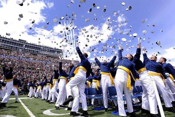 A group of people in uniform throwing caps into the air at a stadium.
