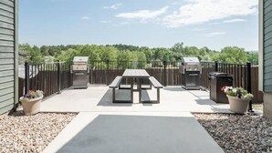 An outdoor patio with a picnic table, two barbecue grills, and a metal fence. - ★Academy Hideaway With View! Sleeps 4 with AC!★ (Colorado Springs)
