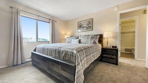 A bedroom with a large bed, a nightstand, a window with curtains, a painting on the wall, and a walk-in closet. - ★Academy Hideaway With View! Sleeps 4 with AC!★ (Colorado Springs)