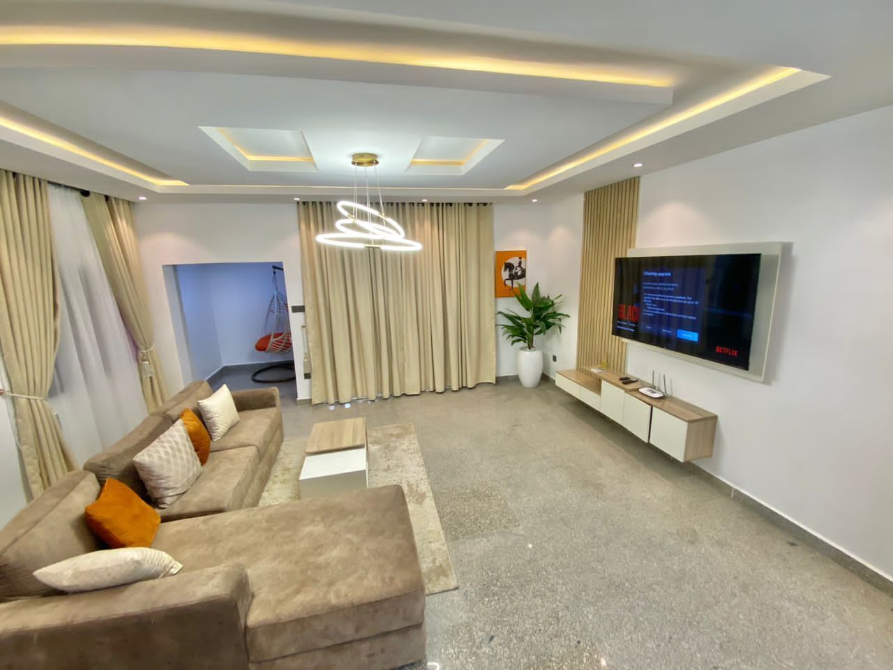 A modern living room with a sofa set, a TV, and a ceiling light fixture.