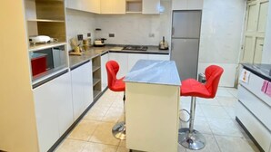 A modern kitchen with white cabinets, a marble countertop, and two red bar stools. - TAOhomes (Abuja)