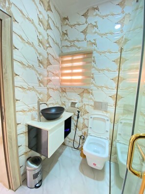 A compact bathroom with a marble backsplash, a black basin, a white toilet, and a trash bin.