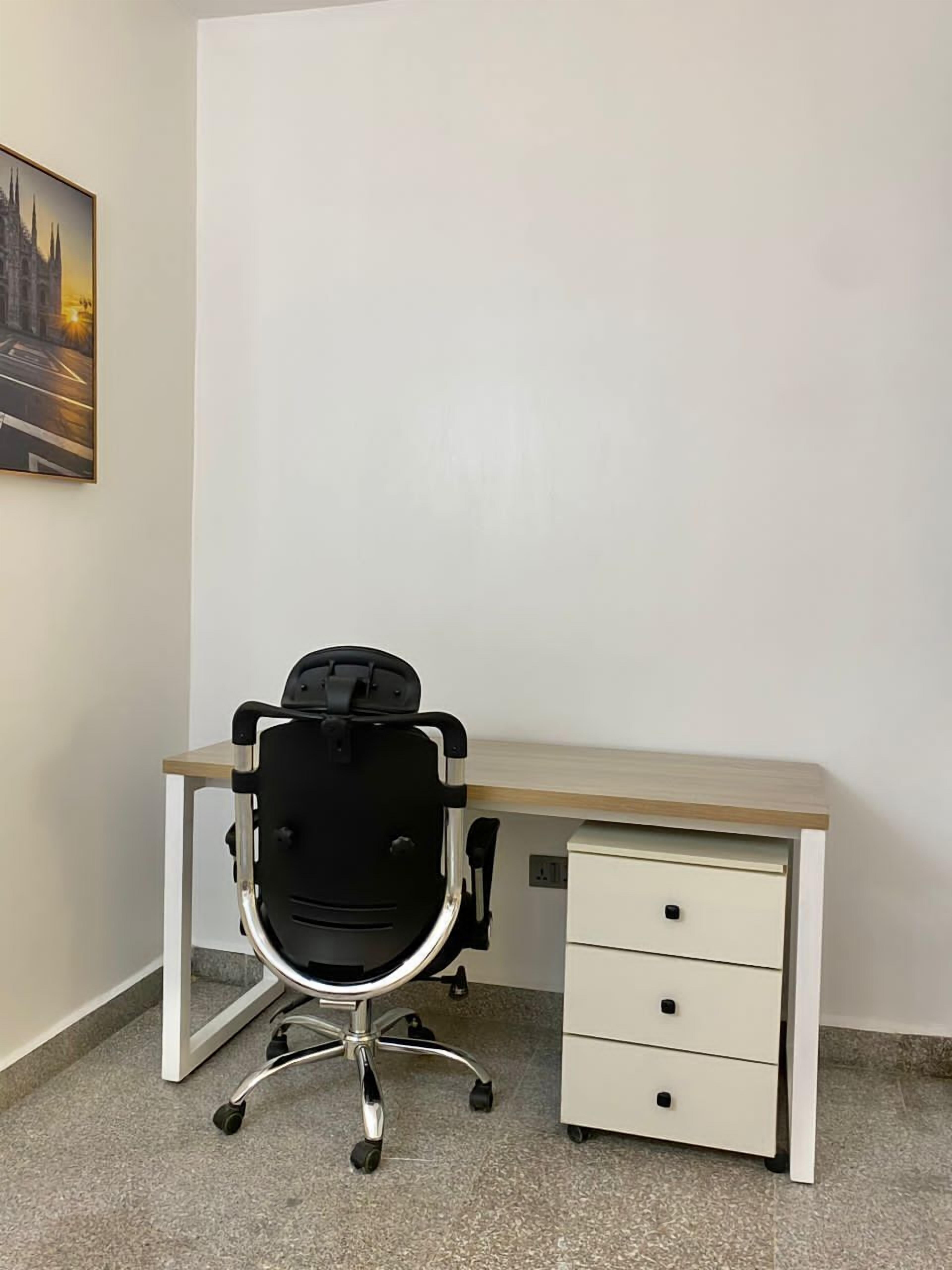 A small office space with a desk and a chair, a white wall, and a framed picture on the wall.