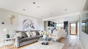 A spacious living room with a grey sofa, a glass coffee table, and a large painting on the wall. -  LONDONERS│Magnificent Londoner  (London)
