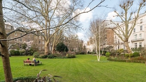 A well-maintained park with a grassy lawn, benches, and mature trees. -  LONDONERS│Magnificent Londoner  (London)