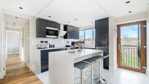 A modern kitchen with a central island, dark cabinetry, and a large window. -  LONDONERS│Magnificent Londoner  (London)