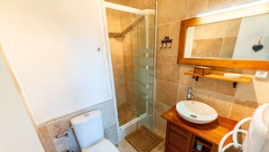 Un bagno con cabina doccia in vetro, un water, un lavabo con mobiletto in legno e uno specchio sopra il lavabo.