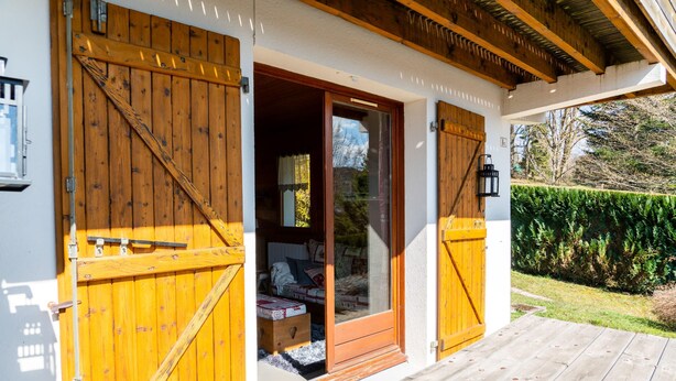 Una porta in legno con un vetro, una panca di legno e vista su un giardino.