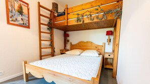 Un letto a castello in legno con una scaletta, un comodino con una lampada rossa e uno scaffale a parete con piante.