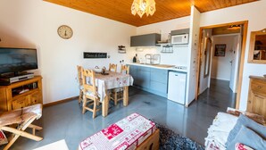 Un accogliente soggiorno con televisione, arredi in legno, un tavolo da pranzo con sedie e un angolo cottura con elettrodomestici moderni.