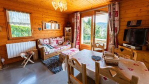 Un accogliente chalet dall'interno in legno, con un divano decorato con cuscini fantasia, un tavolo da pranzo e un televisore.