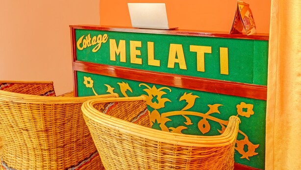 Ein Empfangstisch mit einem Laptop, Korbstühlen und einem Schild mit der Aufschrift 'College MELATI'.