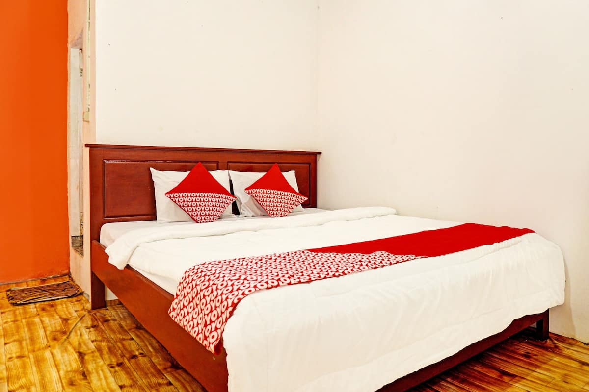 A neatly made bed with white and red bedding, a wooden headboard, and a red throw blanket.