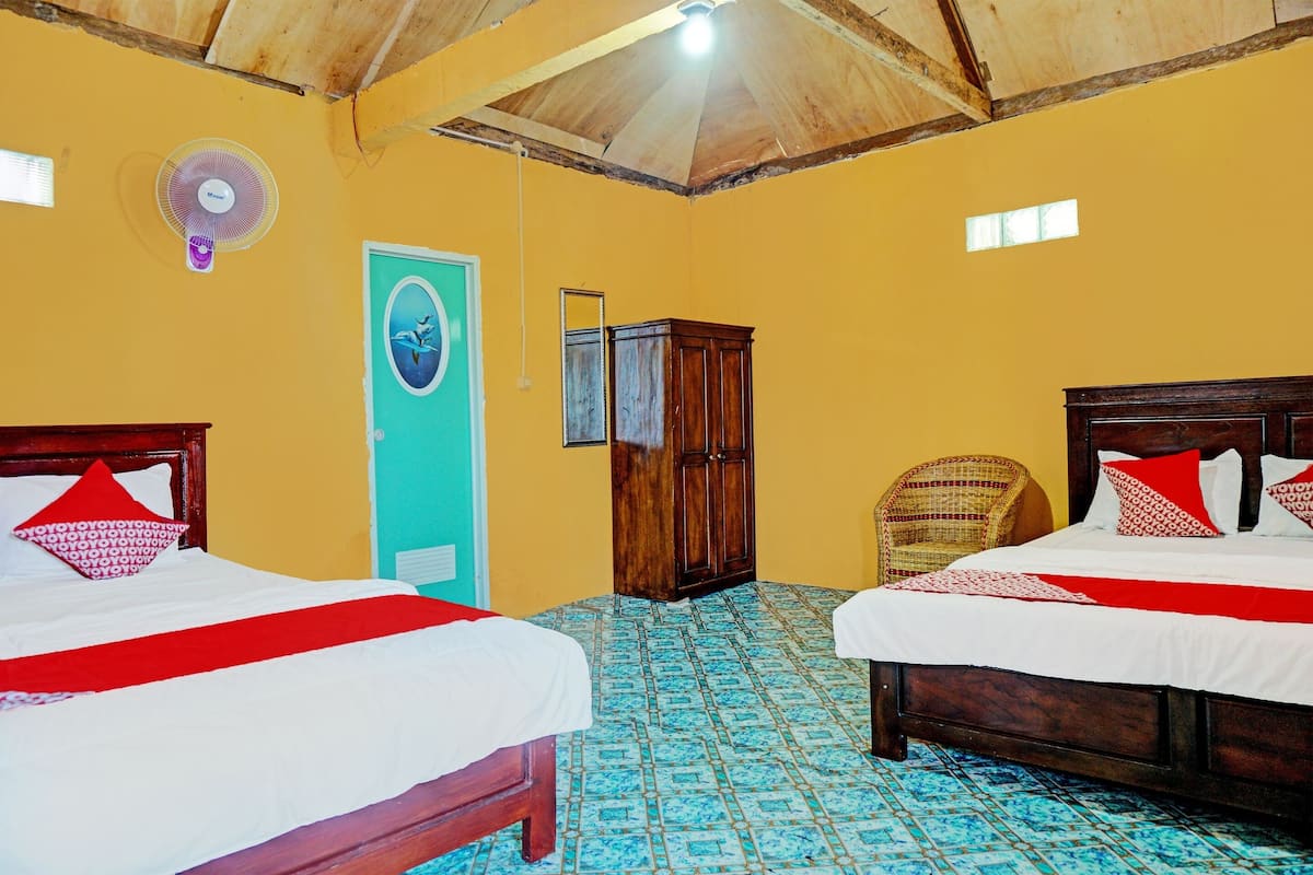 A room with two beds, a wooden ceiling, a fan, a door with a mirror, and a patterned floor.