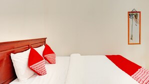 Ein ordentlich bezogenes Bett mit weißer und roter Bettwäsche, ein hölzerner Kopfteil und ein gerahmtes Bild an der Wand.