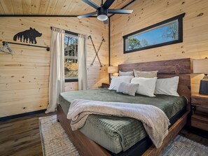 Une chambre de style cabane en bois, avec un lit, un ventilateur de plafond, une fenêtre avec des rideaux et la silhouette d’un ours sur le mur.