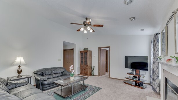 A living room with a leather sofa, a glass coffee table, a ceiling fan, a flat-screen TV, and a fireplace. - FALOLA ESTATES: Live in heaven on earth in our beautiful home (Indianapolis)