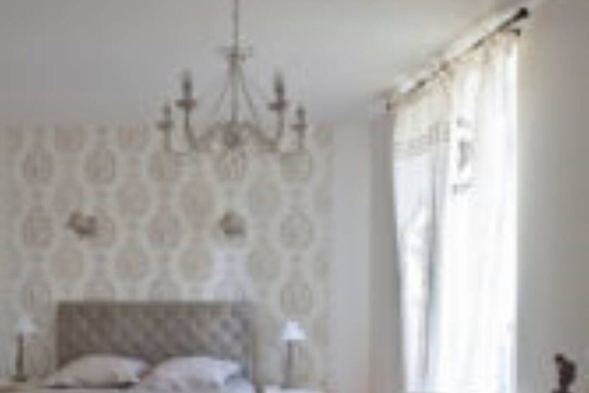 Een slaapkamer met een bed, een stoel, een nachtkastje en een kroonluchter.