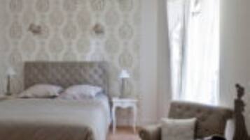 A bedroom with a bed, a chair, a nightstand, and a chandelier.