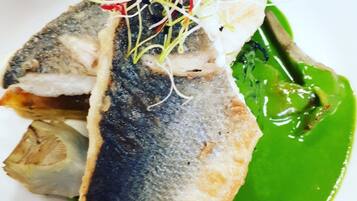A plate with a piece of grilled fish, a slice of bread, and a green sauce.