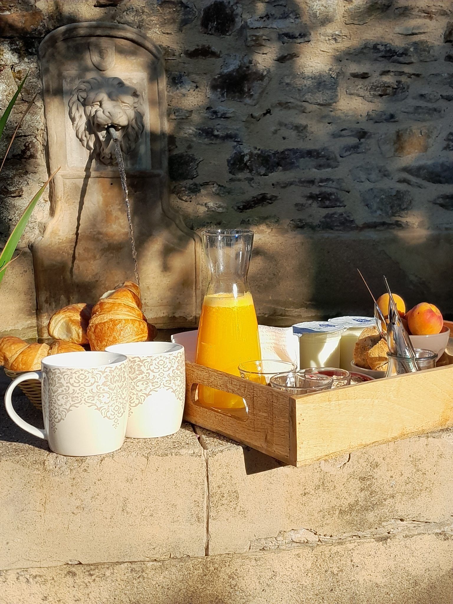 A breakfast tray with croissants, coffee cups, a glass of orange juice, and a fruit bowl.