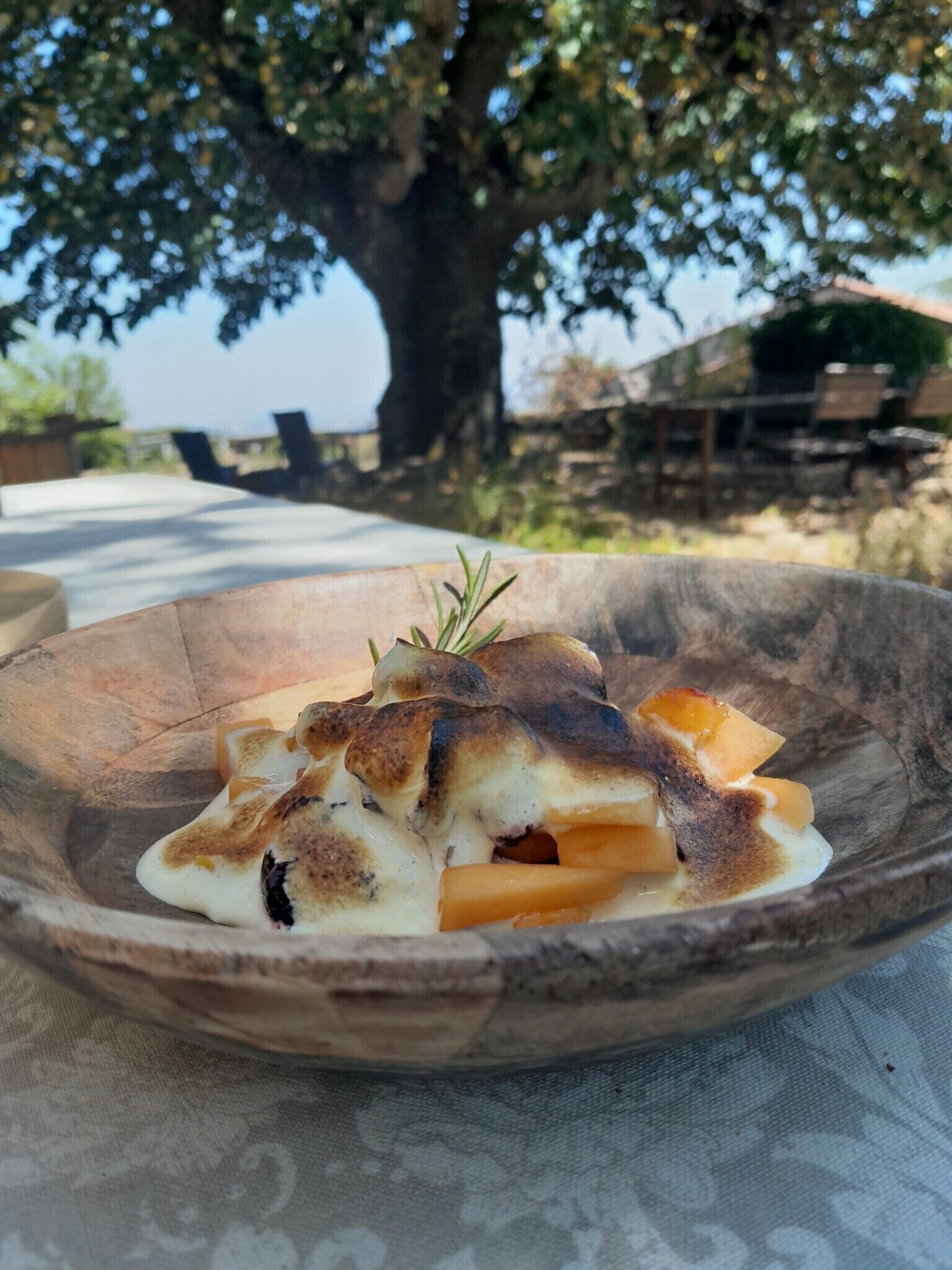 Ein Dessert in einer rustikalen Schüssel auf einem Tisch. Im Hintergrund sind ein Baum und Gartenmöbel zu sehen.