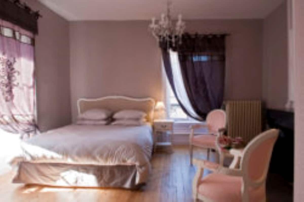 Een slaapkamer met een groot bed, een nachtkastje, een stoel en een raam met gordijnen.