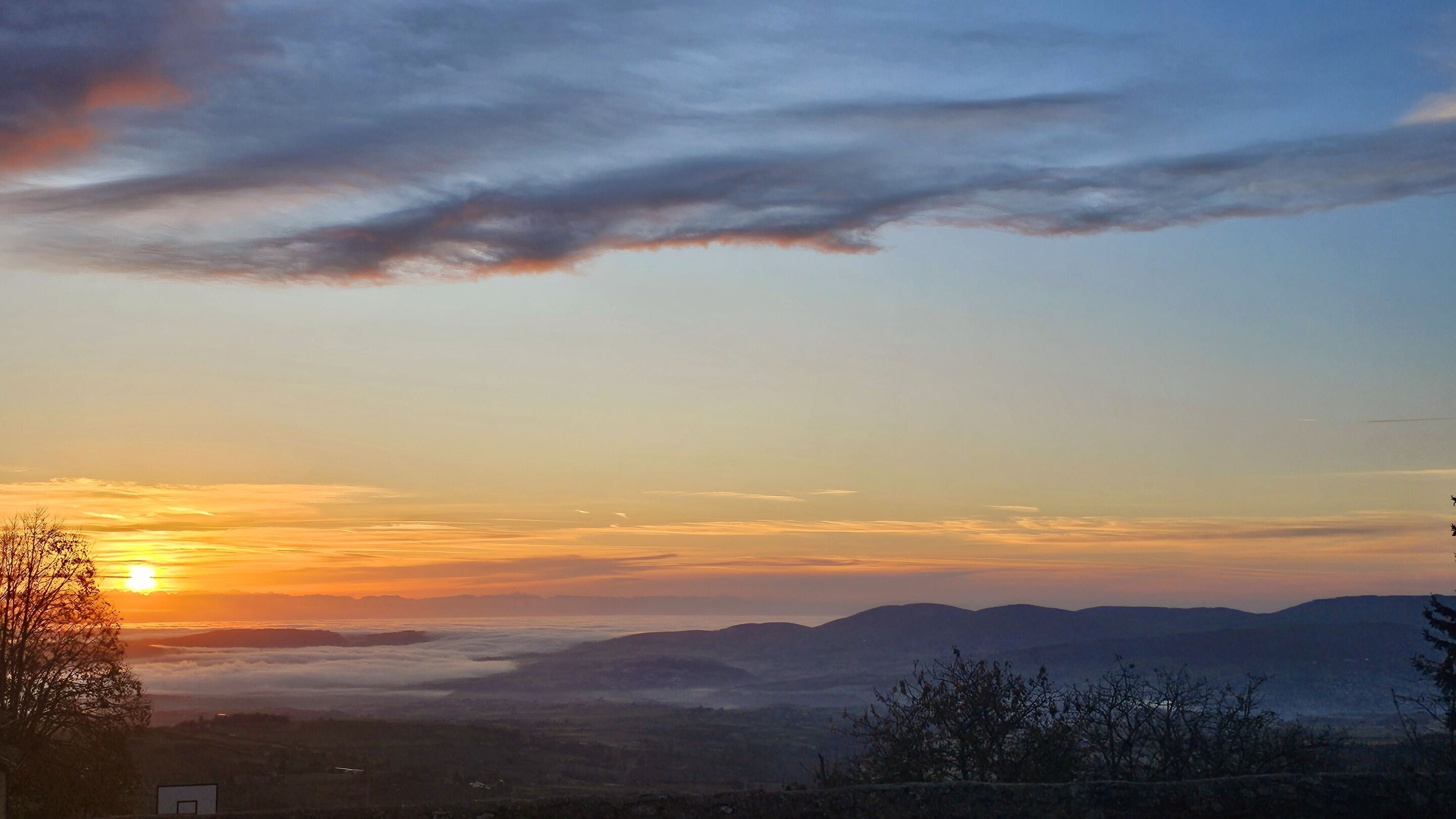 Atardecer sobre un paisaje montañoso con cielo despejado y una cancha de baloncesto visible en primer plano.