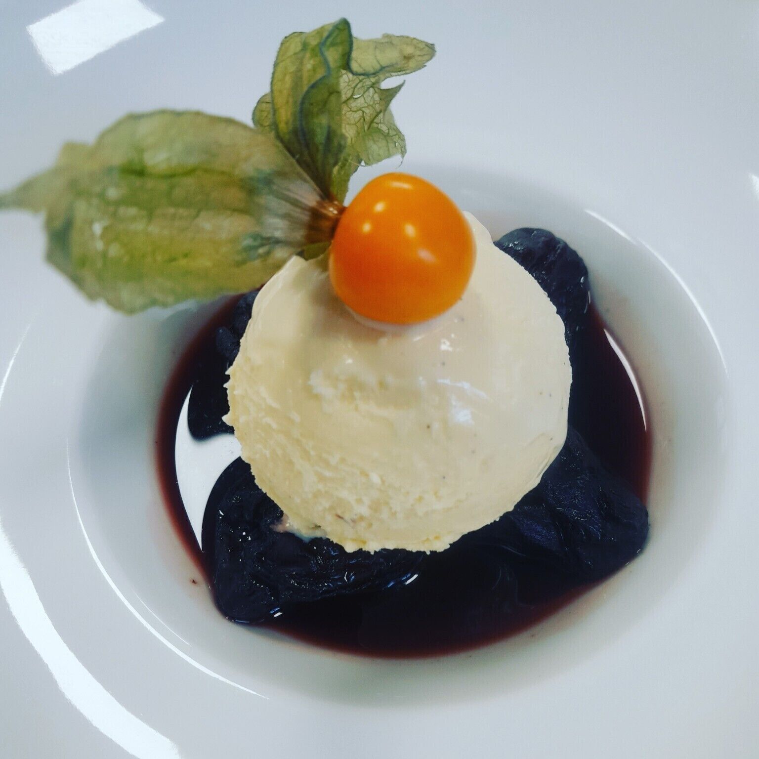 Dessert mit einer Kugel Eis, belegt mit einer Kirsche, serviert auf einem dunklen Teller mit Sauce.