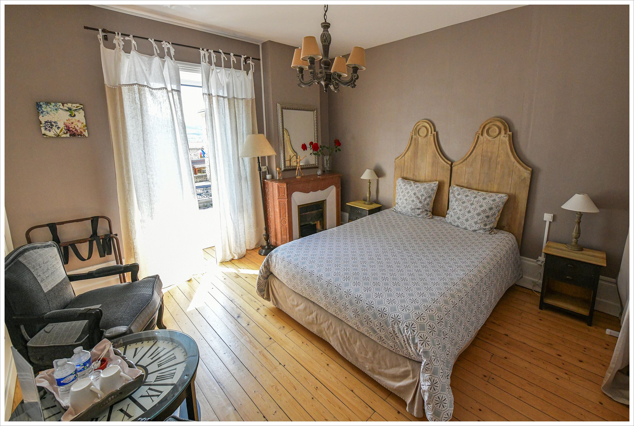 Une chambre à coucher avec un grand lit, une commode en bois, une chaise et une petite table sur laquelle se trouve une horloge.